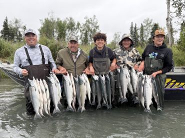 A group of anglers proudly displaying their catch of Salmon while standing in a river, showcasing a successful fishing trip.