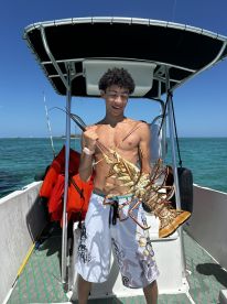 A young angler proudly displaying a large lobster while on a boat in clear waters, showcasing a successful day of fishing.