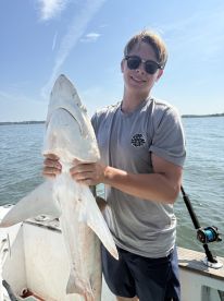 A young angler proudly displaying a large shark while fishing on a sunny day.