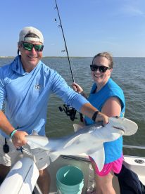 Two anglers proudly displaying a caught shark while fishing on a boat in a coastal environment.