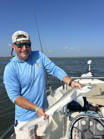 An angler proudly displaying a large shark caught while fishing in a coastal waterway, showcasing the excitement of a successful day on the water.
