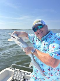 Angler proudly displaying a caught shark while on a fishing boat in a coastal environment.