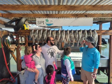 A family joyfully poses in front of a catch board displaying several fish after a successful fishing trip at South Padre Island.
