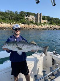 Angler proudly displaying a large Striped Bass while on a fishing trip, with a scenic coastal backdrop.