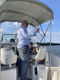 A man operating the helm of a fishing boat, showcasing the interior setup with a clear view of the water and surrounding landscape.