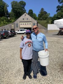 Two individuals posing together with a bucket, likely after a fishing trip, in a parking area near a fishing facility.