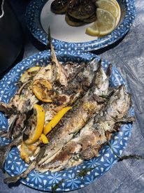 Grilled fish served on a decorative plate, accompanied by lemon slices and grilled lemons, showcasing a delicious catch from a recent fishing trip.