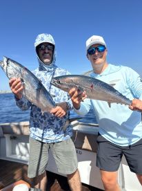Two anglers proudly displaying their catches of fresh Tuna aboard a fishing charter in clear blue waters.