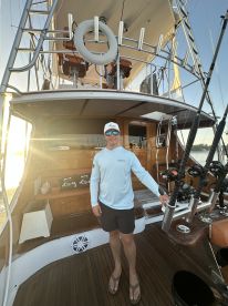 A young man stands inside a well-appointed fishing boat, showcasing the helm and seating area, ready for a day of fishing.