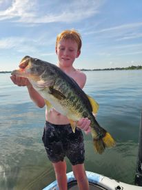 A young angler proudly displaying a large Largemouth Bass while fishing on a calm lake.