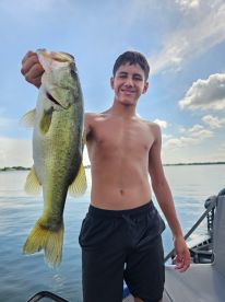 A young angler proudly displaying a large Largemouth Bass while fishing on a calm lake.