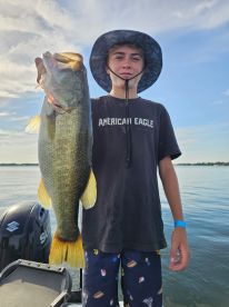 A young angler proudly displaying a large Largemouth Bass while fishing on a calm lake, showcasing a beautiful summer day.