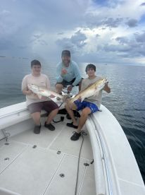 Two young anglers proudly displaying their catches of Redfish while enjoying a day on the water.
