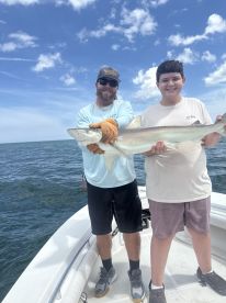 A young angler and an adult proudly displaying a caught shark while on a fishing charter in open waters.