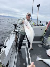 An angler proudly displaying a large Halibut aboard a fishing boat in open waters, showcasing a successful day of deep-sea fishing.