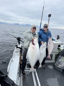 Two anglers proudly displaying their catch of large Halibut while fishing on a boat in open waters, showcasing a successful day of fishing.