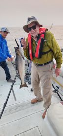 An angler proudly displaying a large salmon while fishing on a boat, with another person assisting in the background.