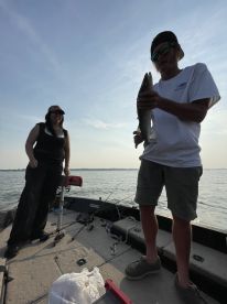 Two anglers enjoying a sunny day on the water, with one proudly displaying a caught fish on a fishing boat.