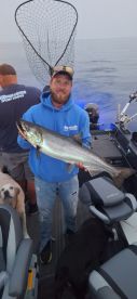 Angler proudly displaying a large fish on a boat during a fishing trip, with a scenic ocean backdrop.