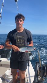 A young angler proudly displaying a caught fish while aboard a fishing boat in open waters.