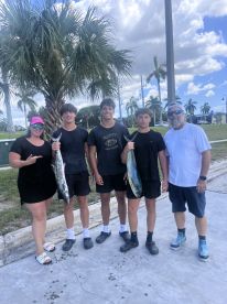 A family proudly displaying their catch of Mahi Mahi after a successful fishing trip, set against a backdrop of palm trees.