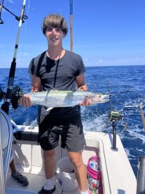 A young angler proudly displaying a large fish while aboard a fishing boat in open waters.