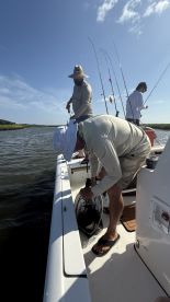 Anglers actively fishing from a boat, with rods in hand and a net being used to catch fish in a scenic waterway.