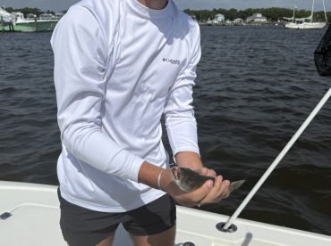 A young angler holding a small fish while fishing from a boat, showcasing a successful catch in a scenic waterway.