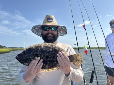 An angler proudly displaying a Flounder while fishing in a scenic coastal marsh environment.