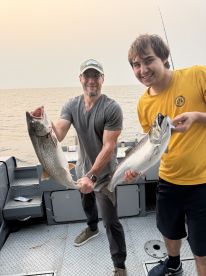 Two anglers proudly displaying their catches of Lake Trout aboard a fishing boat, enjoying a successful day on the water.