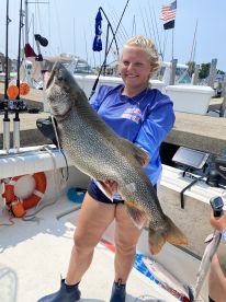 A young angler proudly displaying a large Lake Trout on a fishing boat, showcasing a successful day on the water.