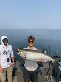 A young angler proudly displays a large Salmon while fishing on a boat, showcasing a successful day on the water.