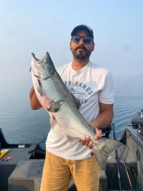 An angler proudly displaying a large Salmon while fishing on a calm lake, showcasing a successful day on the water.