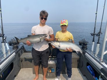 Two young anglers proudly displaying their catches of Salmon while fishing on a boat, showcasing a successful day on the water.