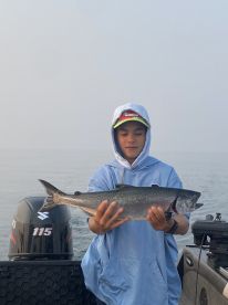 Young angler proudly holding a large salmon while fishing on a calm morning.