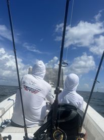 Two anglers in white hoodies seated inside a fishing boat, enjoying a day on the water with fishing rods ready.