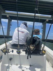 Two anglers seated inside a small boat, preparing for fishing under a bridge, showcasing a casual fishing environment.
