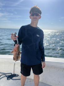 Young angler proudly displaying a freshly caught Grouper while fishing on a sunny day.
