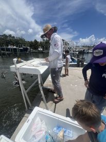 A family enjoys a day at the dock, with a cooler filled with freshly caught fish, while a man prepares for the next step in their fishing adventure.