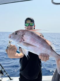 A young angler proudly displaying a large Snapper while fishing offshore, showcasing a sunny day on the water.
