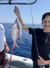 A young angler proudly displaying a large Snapper while fishing on a boat in open waters.