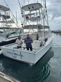 Two anglers posing with thumbs up on the 'Sweet Dreams' boat at the marina, showcasing the vessel's exterior and fishing readiness.