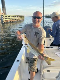 Angler proudly displaying a Snook caught while fishing near a bridge, showcasing a sunny day on the water.