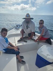 A family enjoying a fishing trip on a boat, with two young boys assisting an adult in handling a small shark.