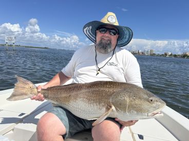 An angler proudly displaying a large Redfish while fishing in a scenic coastal environment.