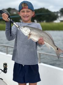A young angler proudly displaying a Redfish while fishing on a boat, showcasing a fun day on the water.