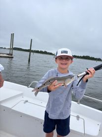 A young angler proudly displaying a Speckled Trout while fishing on a cloudy day.