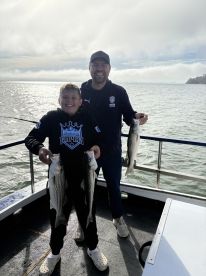 A young angler and an adult proudly displaying their catch of striped bass while fishing on a boat, showcasing a joyful moment on the water.