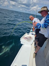 Two anglers actively reeling in a fish while fishing offshore, showcasing the excitement of the catch.