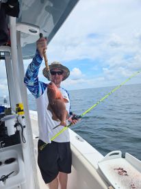 Angler proudly displaying a large Red Snapper while fishing on a boat in open waters.
